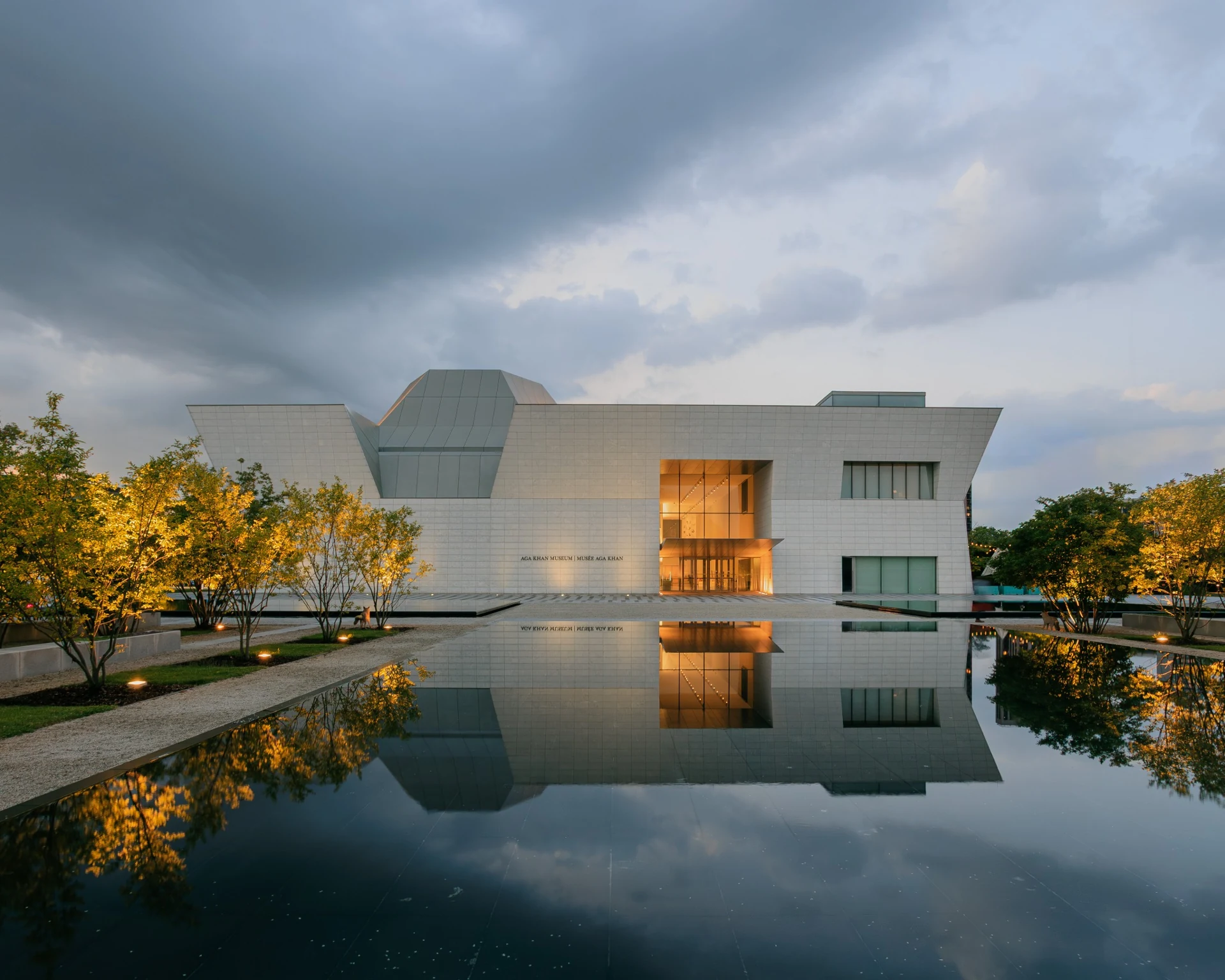 Aga Khan Museum at dusk, reflected in a still pool beneath a dramatic sky